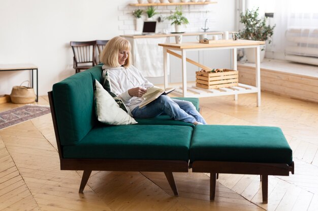 Ältere Frau, die ein Buch zu Hause auf Sofa liest