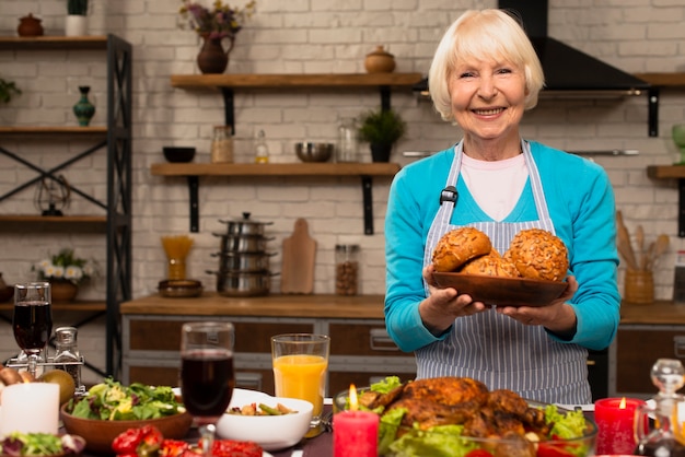 Ältere Frau, die eine Platte mit Brot hält und Kamera betrachtet