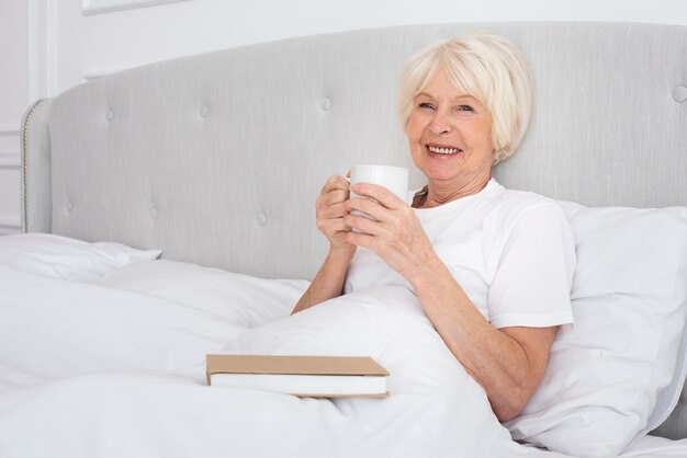 Ältere Frau, die eine Tasse im Schlafzimmer liest