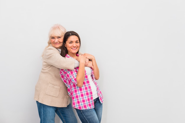 Ältere Frau, die ihre lächelnde Tochter gegen weißen Hintergrund umarmt