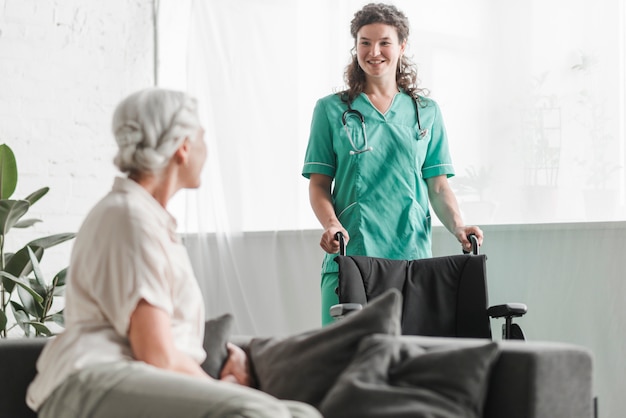 Ältere Frau, die lächelnde weibliche Krankenschwester mit Rollstuhl betrachtet