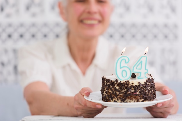 Ältere Frau, die Platte des köstlichen Geburtstagskuchens mit glühenden Zahlkerzen hält