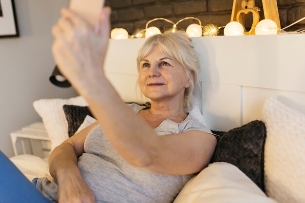 Ältere Frau, die selfie auf Bett nimmt