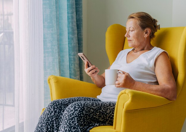 Ältere Frau, die Smartphone zu Hause während der Pandemie beim Kaffee verwendet