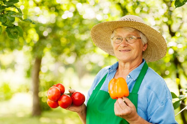 Ältere Frau, die Tomaten und gelben Pfeffer hält