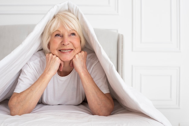 Ältere Frau, die unter Decke sitzt