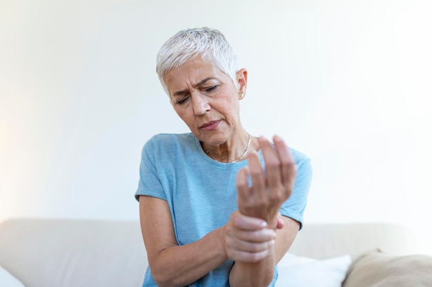 Ältere Frau, die unter Schmerzen in der Hand Arthritis leidet, alte Person und ältere Frau, die zu Hause unter Schmerzen leidet