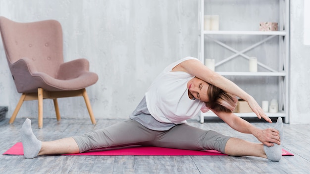 Ältere Frau, die Yoga im Wohnzimmer ausdehnend tut