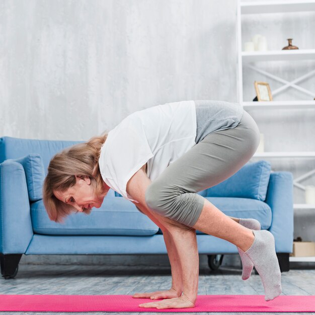 Ältere Frau, die Yoga im Wohnzimmer tut