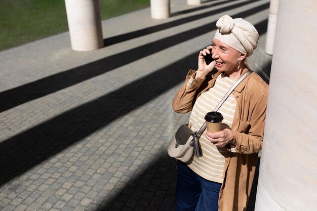 Ältere Frau draußen in der Stadt, die beim Kaffee telefonieren