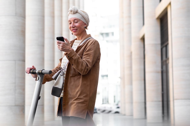 Ältere Frau mit einem Elektroroller in der Stadt mit Smartphone