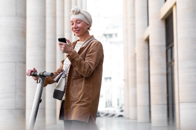 Ältere Frau mit einem Elektroroller in der Stadt mit Smartphone