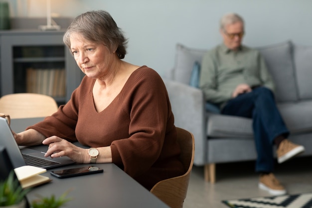 Ältere Frau mit Laptop sitzt am Schreibtisch im Wohnzimmer