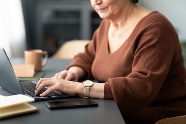 Ältere Frau mit Laptop sitzt am Schreibtisch im Wohnzimmer