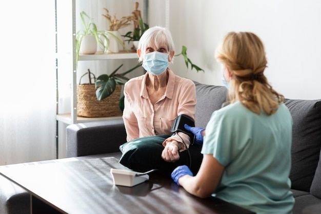 Ältere Frau mit medizinischer Maske, die ihren Blutdruck im Pflegeheim überprüfen lässt