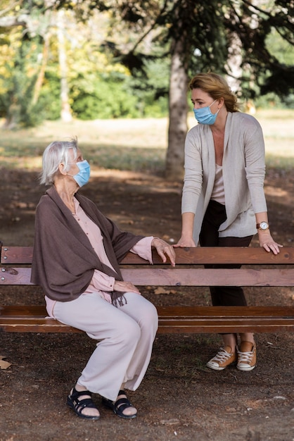 Ältere Frau mit medizinischer Maske im Gespräch mit Frau auf der Bank