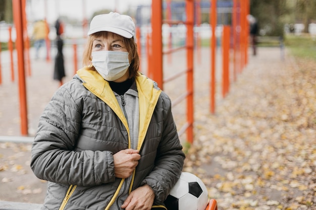 Ältere Frau mit medizinischer Maske und Fußball im Freien