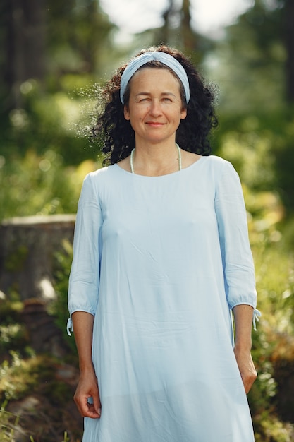 Ältere Frau schaut in die Kamera. Dame in einem blauen Kleid. Brünette geht.