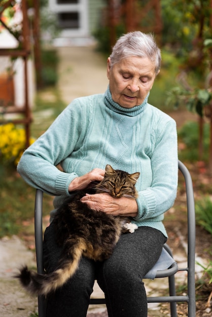 Ältere Frau sitzt auf Stuhl und streichelt Katze