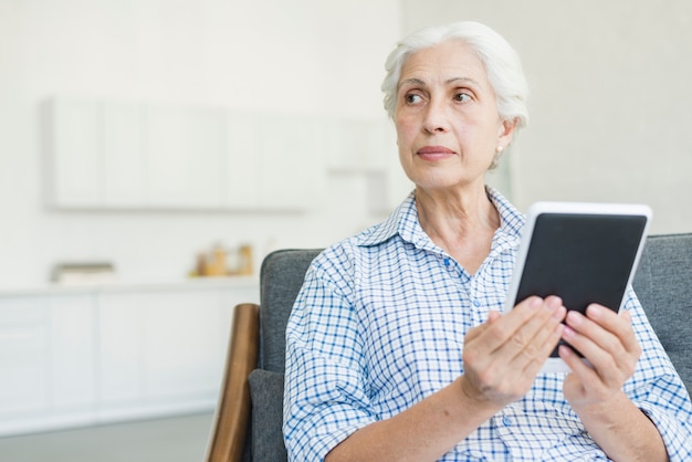 Ältere Frau, welche die digitale Tablette weg schaut hält