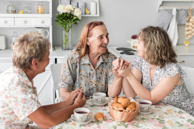 Ältere Frau, welche die Hand ihrer Tochter und der großartigen Tochter während des Frühstücks hält