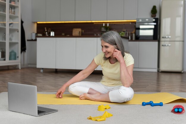 Ältere Frau zu Hause, die Fitnessunterricht auf dem Laptop nimmt