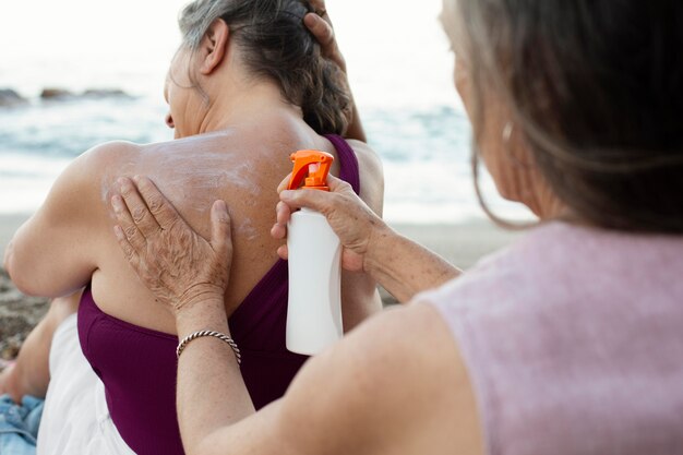 Ältere Frauen, die Sonnencreme auf der Rückseite am Strand auftragen