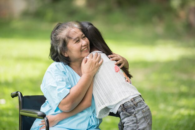 Ältere Großmutter im Rollstuhl mit Enkelin im Krankenhausgarten