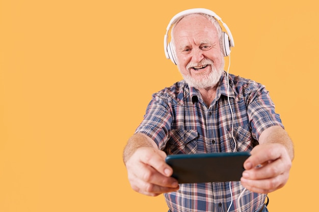 Ältere hörende Musik des smiley des niedrigen Winkels auf Mobile