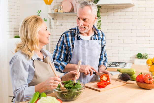 Ältere Paare, die den Salat in der modernen Küche sich gegenseitig betrachten