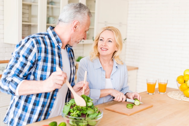 Ältere Paare, die einander zubereiten, das Lebensmittel in der Küche zubereitend