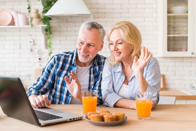 Ältere Paare, die ihre Hände während des on-line-Videoanrufs auf Laptop wellenartig bewegen