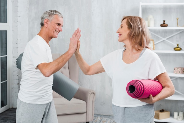 Ältere Paare, welche die Yogamatten geben, die Hoch fünf geben