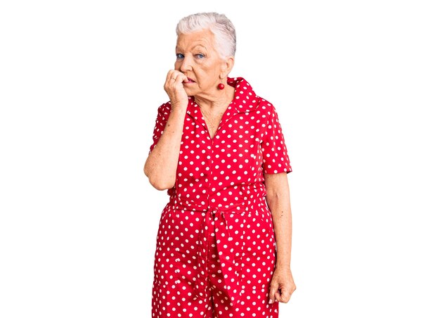 Ältere schöne Frau mit blauen Augen und grauen Haaren, die ein rotes Sommerkleid trägt, sieht gestresst und nervös aus, mit den Händen auf dem Mund, beißenden Nägeln, Angstproblemen