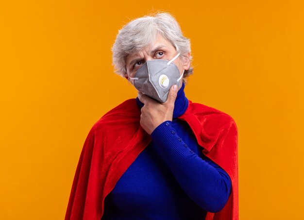 Ältere Superheldin mit rotem Umhang und Gesichtsschutzmaske, die verwirrt über Orange schaut