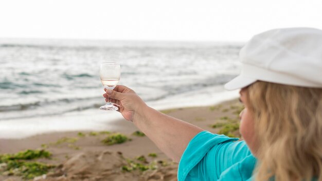 Ältere Touristenfrau, die Glas am Strand hält