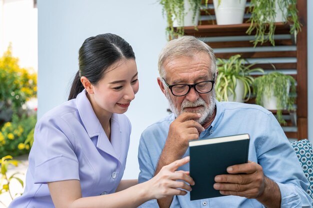 Älterer älterer Mann liest Buch mit Krankenschwester im Garten