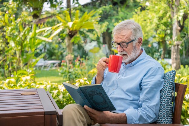 Älterer älterer Mann liest Buch und trinkt Kaffee im Garten