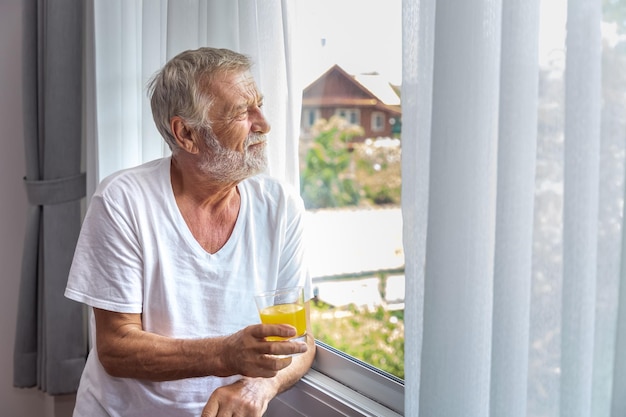 Älterer älterer Mann steht und schaut aus dem Fenster im Schlafzimmer, nachdem er morgens mit Saft aufgewacht ist