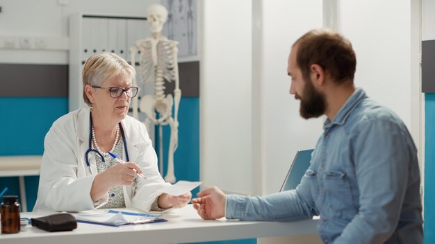 Älterer Arzt und kranker Patient, der an der Gesundheitsuntersuchung im Kabinett teilnimmt und Rezeptpapier erhält, um Behandlung und Medikamente nach Termin zu kaufen. Krankheitsbericht nach Absprache.