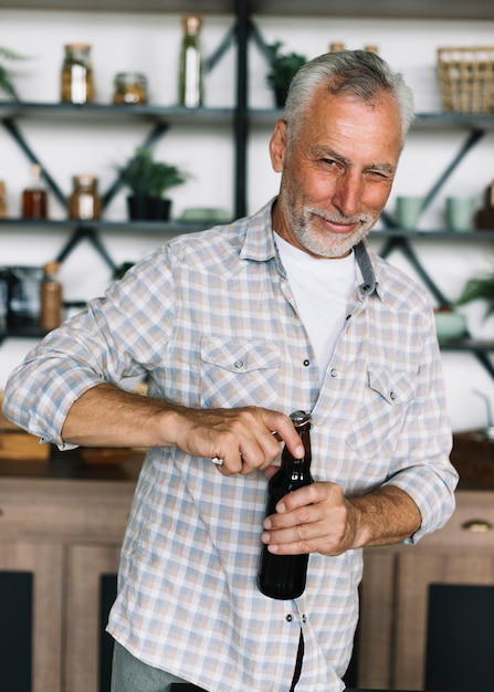 Älterer blinkender Mann beim Öffnen der Kappe der Bierflasche