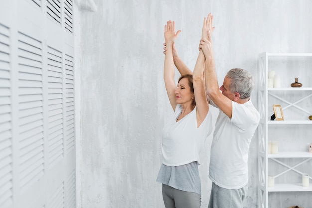 Älterer Ehemann, der seiner Frau hilft, Position des Yoga zu tun
