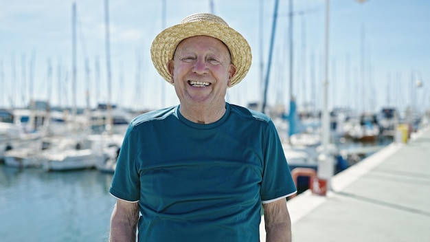 Älterer grauhaariger Tourist mit Sommerhut lächelt im Hafen