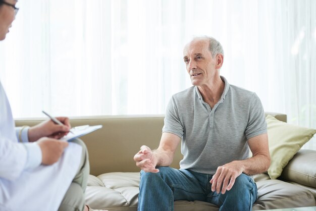 Älterer kaukasischer männlicher Patient, der zu Hause Gesundheitsbeschwerden mit Doktor teilt