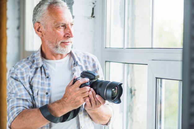 Älterer männlicher Fotograf, der das Fenster hält dslr Kamera betrachtet