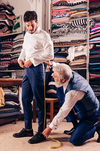Älterer männlicher Modedesigner, der das Bein des Kunden im Shop misst