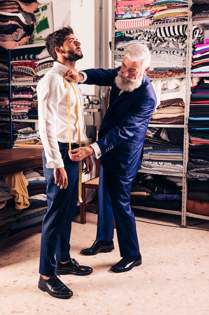 Älterer männlicher Modedesigner, der Maße seines Kunden im Shop nimmt