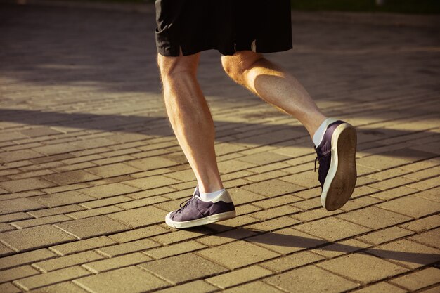 Älterer Mann als Läufer an der Stadtstraße. Nahaufnahme Schuss von Beinen in Turnschuhen. Kaukasisches männliches Model-Joggen und Cardio-Training am Sommermorgen. Gesunder Lebensstil, Sport, Aktivitätskonzept.