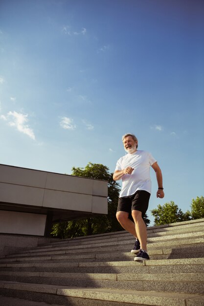 Älterer Mann als Läufer mit Armband oder Fitness-Tracker an der Straße der Stadt. Kaukasisches männliches Model, das am Sommermorgen Joggen und Cardio-Training übt. Gesunder Lebensstil, Sport, Aktivitätskonzept.