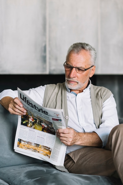 Älterer Mann, der auf Sofa liest Zeitung sitzt